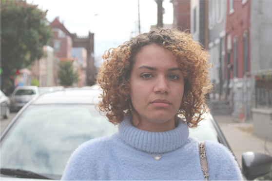 photograph of a girl in a blue sweater standing on a street